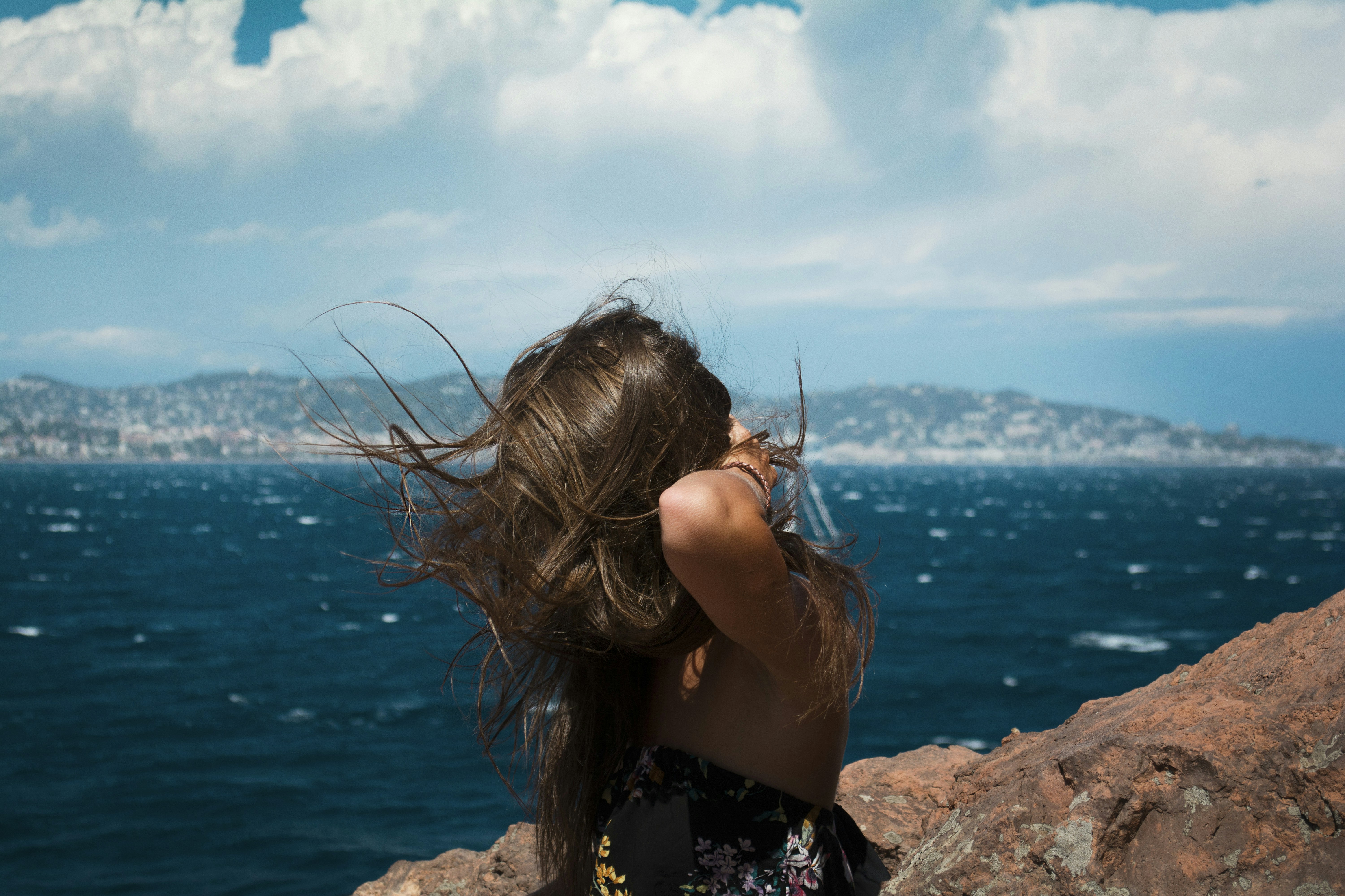 woman in black and white floral dress sitting on rock near body of water during daytime