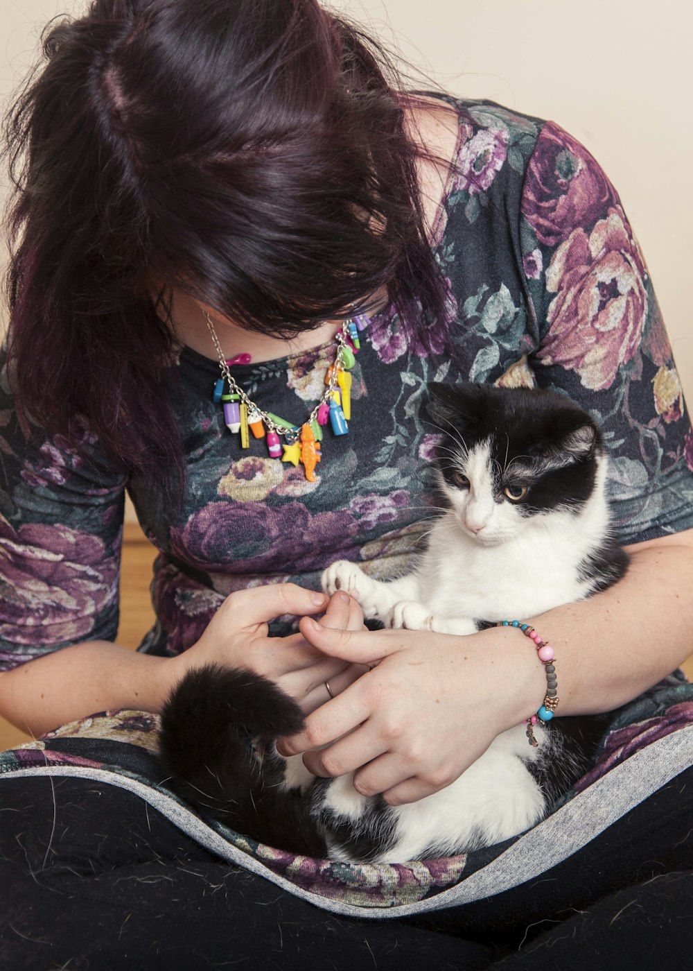 woman in black and pink floral shirt holding white and black cat