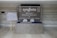 A welcome area with a large sign featuring the logo 'syngenta' and a message for business partners and country leadership team is displayed on a wall. There is a seating plan on a wooden easel to the left, and a table with wrapped items in front of the sign.