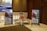 A conference hall with a display featuring two promotional standees showcasing a family in traditional attire, highlighting a product related to agriculture. There is a statue of a man seated with a child on his shoulders and a patterned table. The lighting is warm and the decor includes elegant paneling and chandeliers.