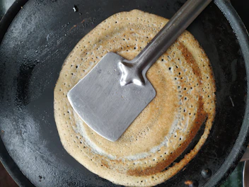 Golden-brown gözleme being cooked on a round black pan over the stove