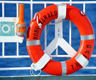 orange and white life buoy hanged on metal fence