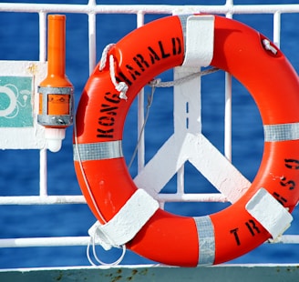 orange and white life buoy hanged on metal fence