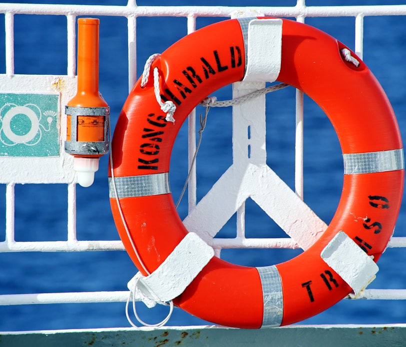 orange and white life buoy hanged on metal fence