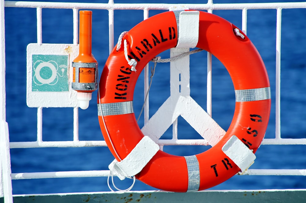orange and white life buoy hanged on metal fence
