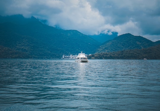 white boat on sea near mountain under white clouds and blue sky during daytime in Sun Moon Lake Taiwan