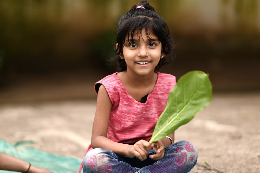 girl in pink shirt and blue denim jeans sitting on ground