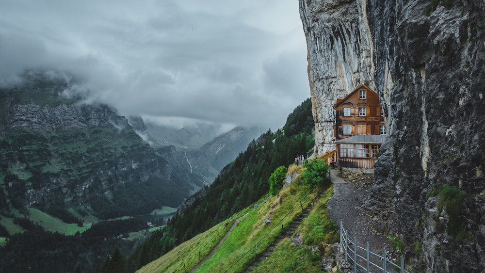 brown wooden house on green grass field near mountain under white clouds during daytime