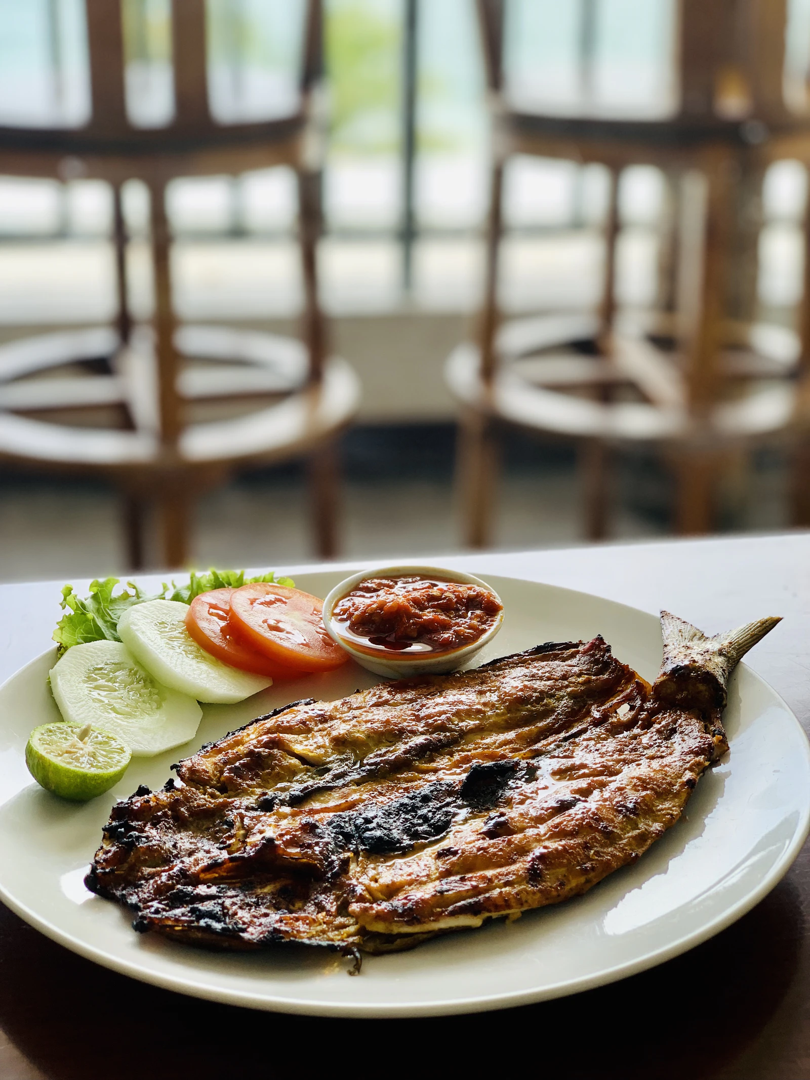 Poisson grillé servi dans une assiette avec crudités, citron vert et sauce