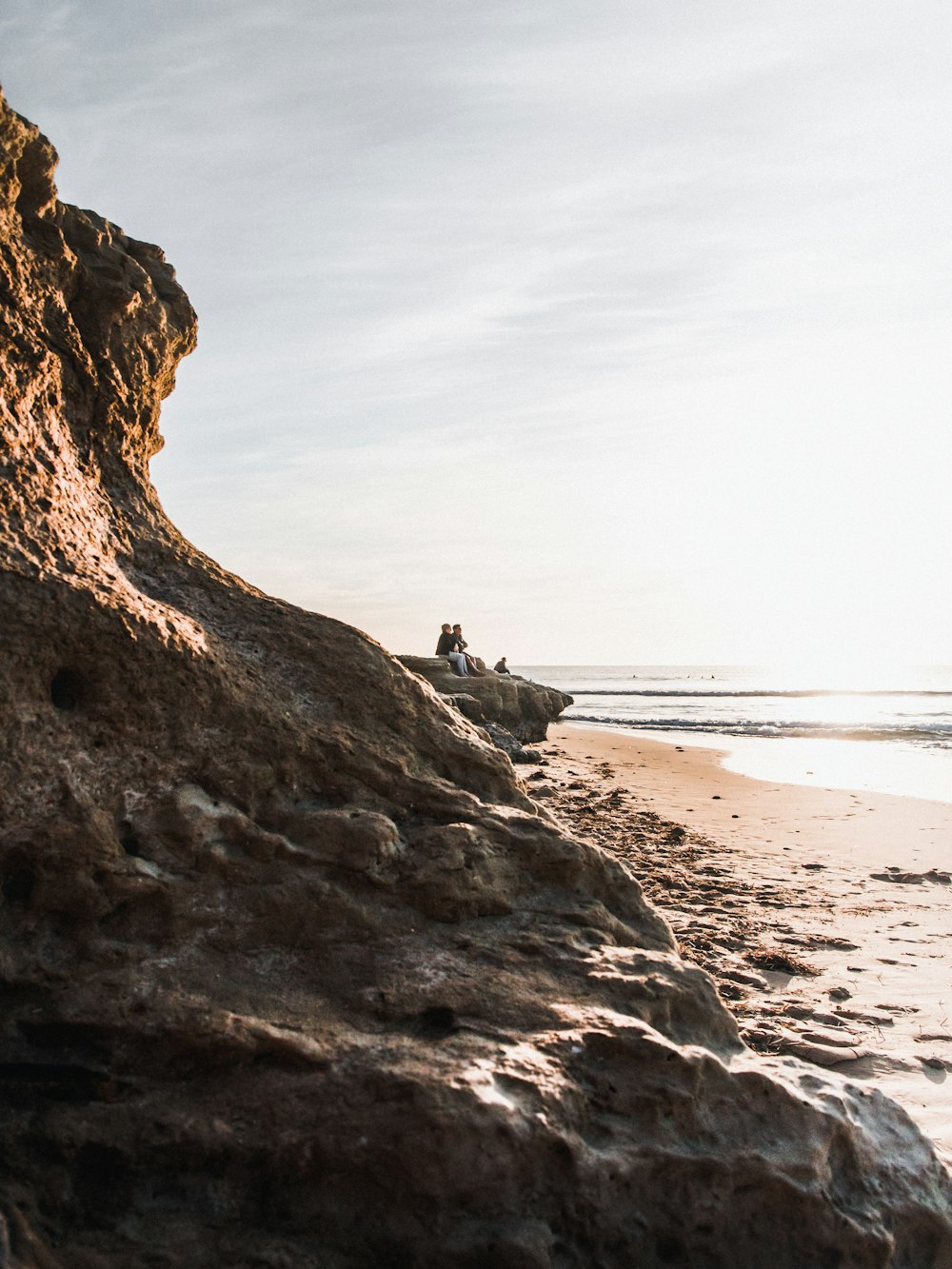 person sitting on rock formation near sea during daytime