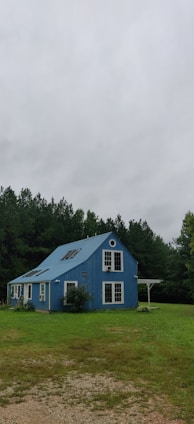 blue wooden house near green trees under white clouds during daytime