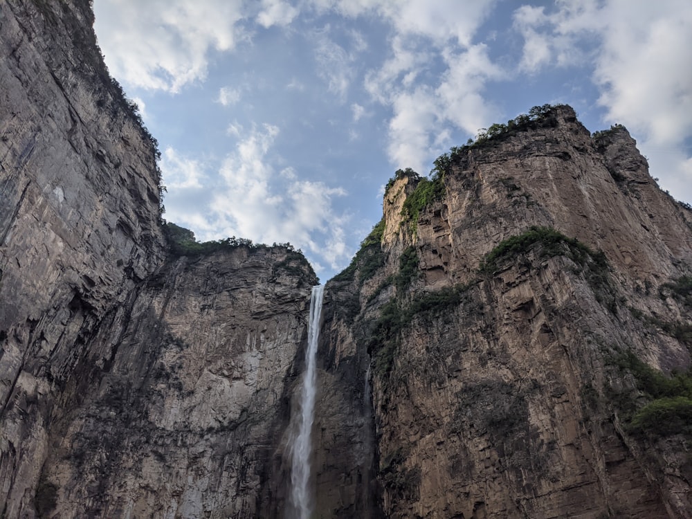 waterfalls on brown rocky mountain under white clouds during daytime