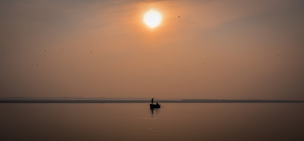 silhueta da pessoa que monta o barco no mar durante o pôr do sol