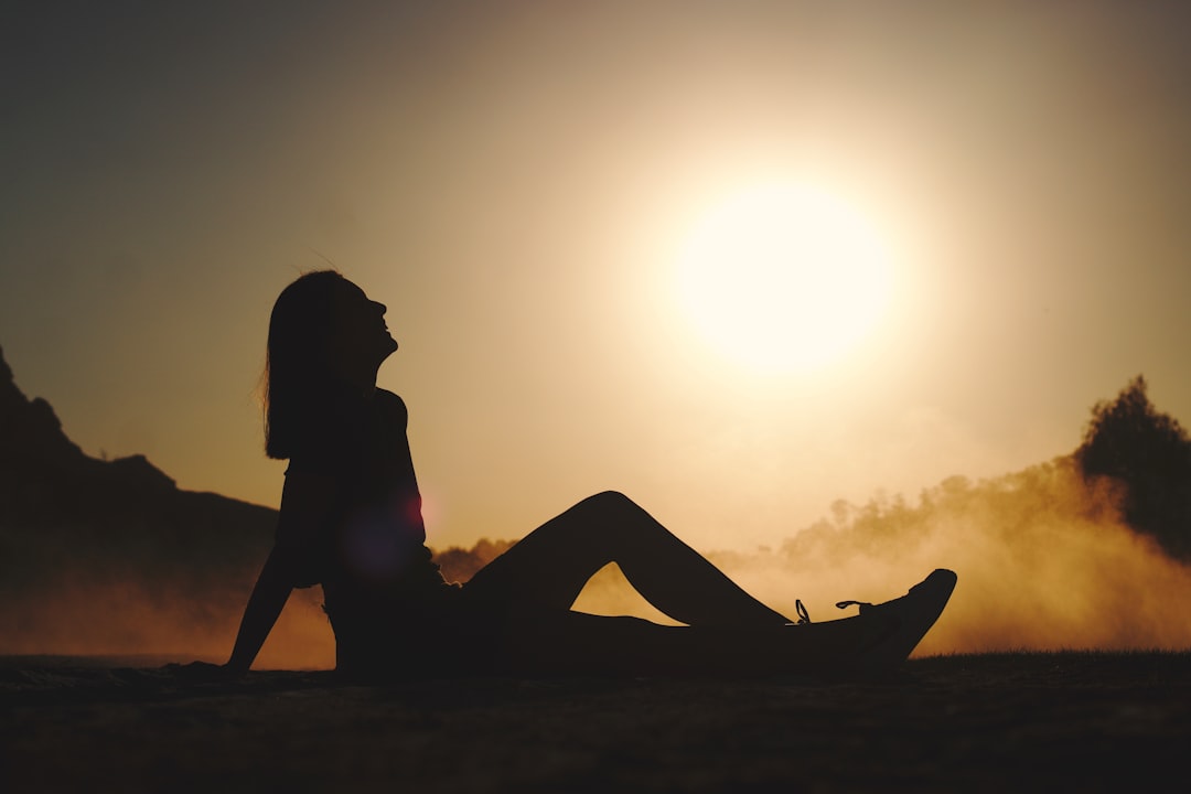 silhouette of woman sitting on sand during sunset