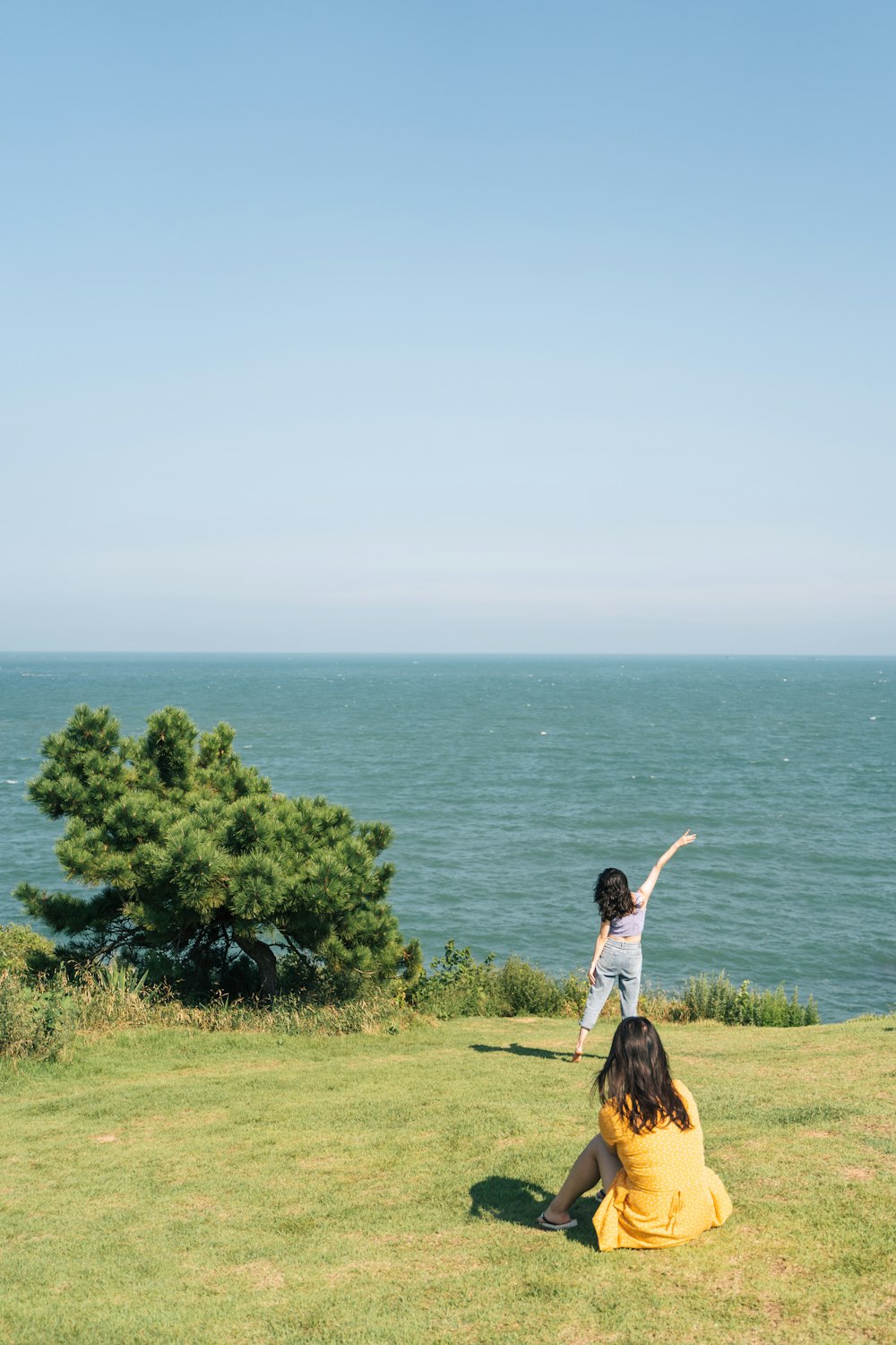 白い長袖シャツを着た女性が、水域の近くの緑の芝生のフィールドに立っている