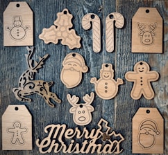Wooden cutouts featuring various Christmas-themed shapes, including snowmen, candy canes, reindeer, holly leaves, a Santa Claus face, and a gingerbread man, arranged on a textured wooden surface. The words 'Merry Christmas' are also carved in wood.