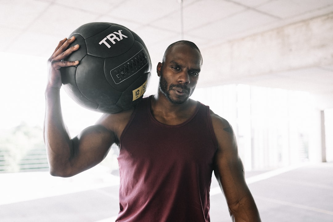 man in red tank top holding black and white soccer ball