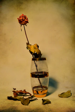 A mysterious woman in Victorian attire arranging dried roses in a black ceramic vase.