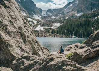 person sitting on rock near lake and mountain range