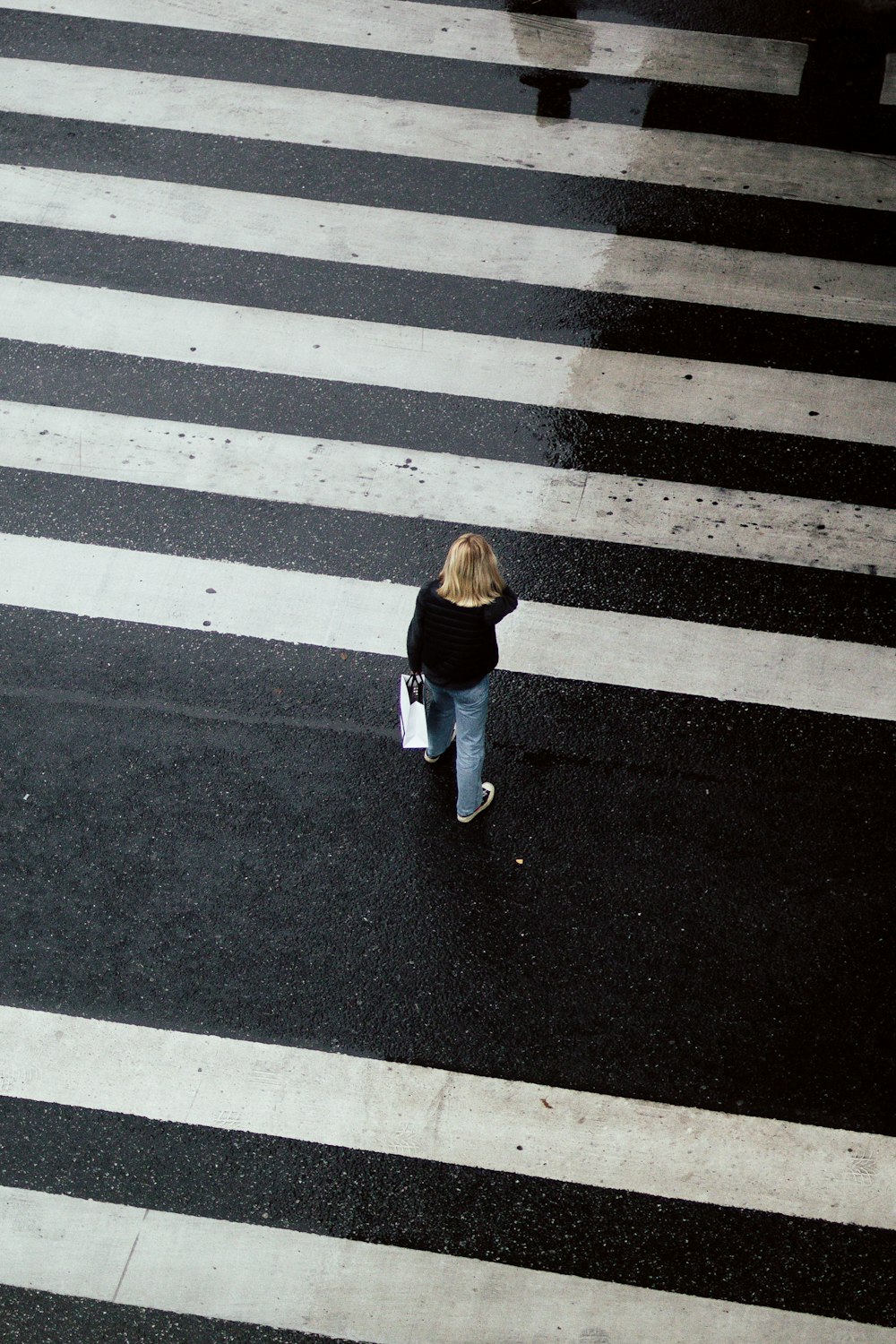 Mujer con chaqueta marrón y pantalones blancos caminando por el carril peatonal