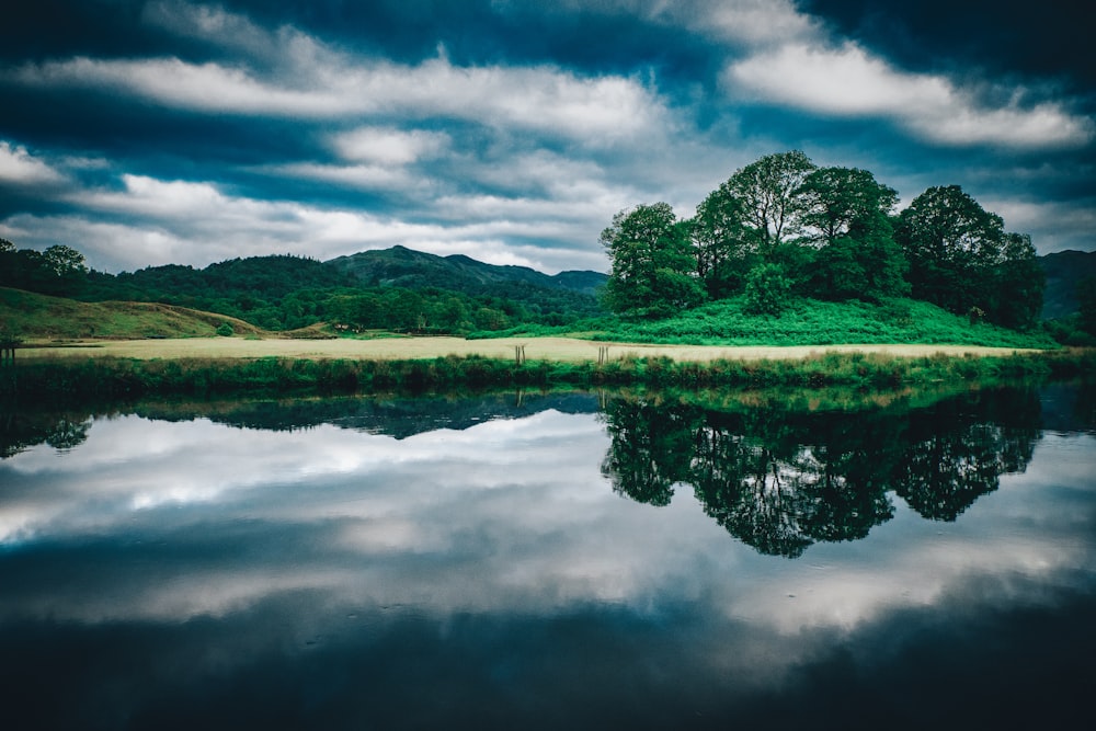 green grass field near lake under cloudy sky during daytime