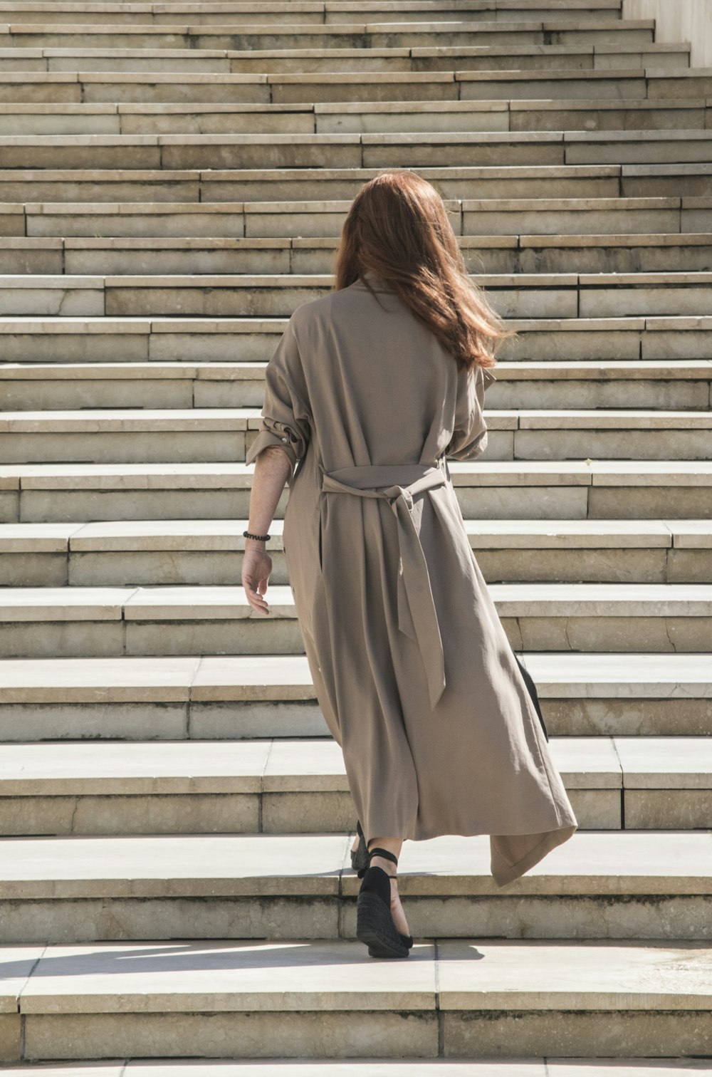 白いコンクリートの階段を歩く茶色の長袖ドレスを着た女性