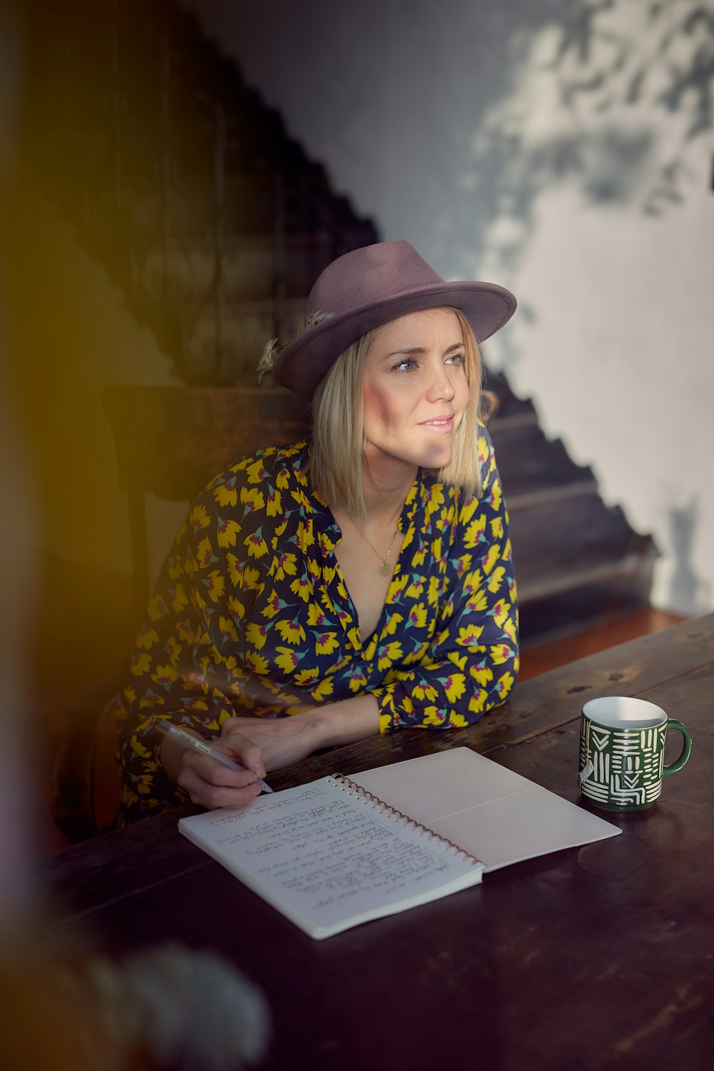 mulher na camisa floral azul e amarela de manga comprida vestindo o chapéu marrom do fedora