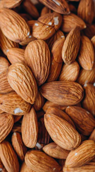 Close-up of seasoned almond slivers spilling from a rustic wooden bowl onto a natural linen cloth.