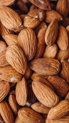 A handful of vibrant almonds held gently against the backdrop of lush green mountain slopes.