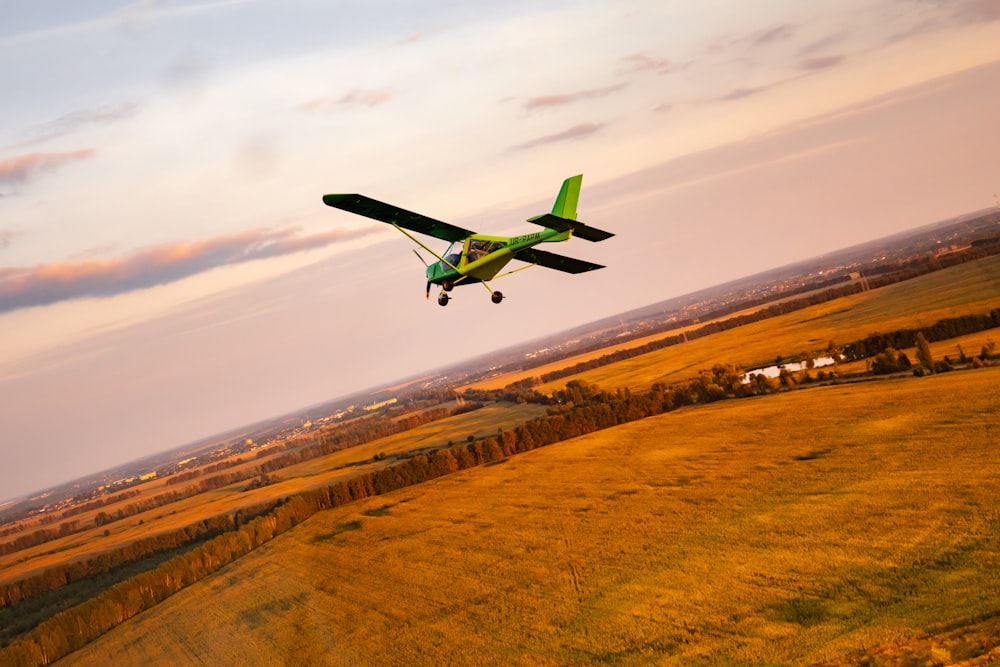 green and black plane flying over brown field during daytime