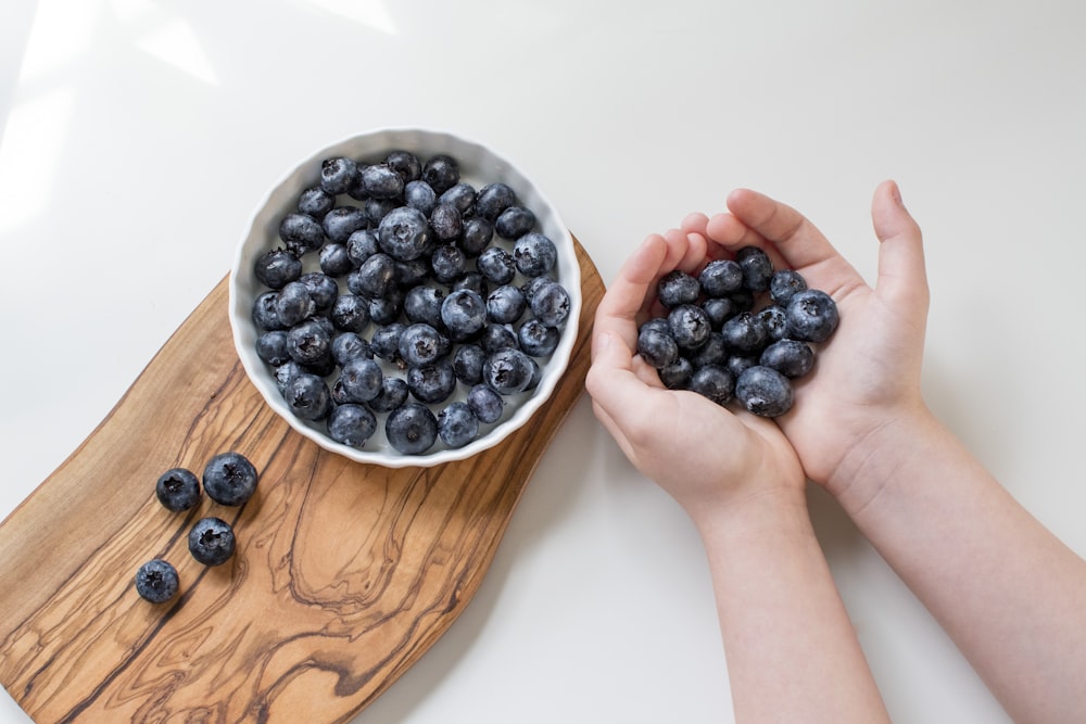 person holding blue berries in white ceramic bowl