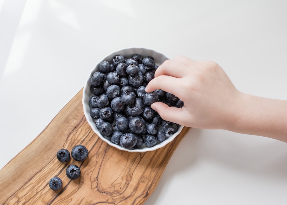 person holding blue berries in white ceramic bowl