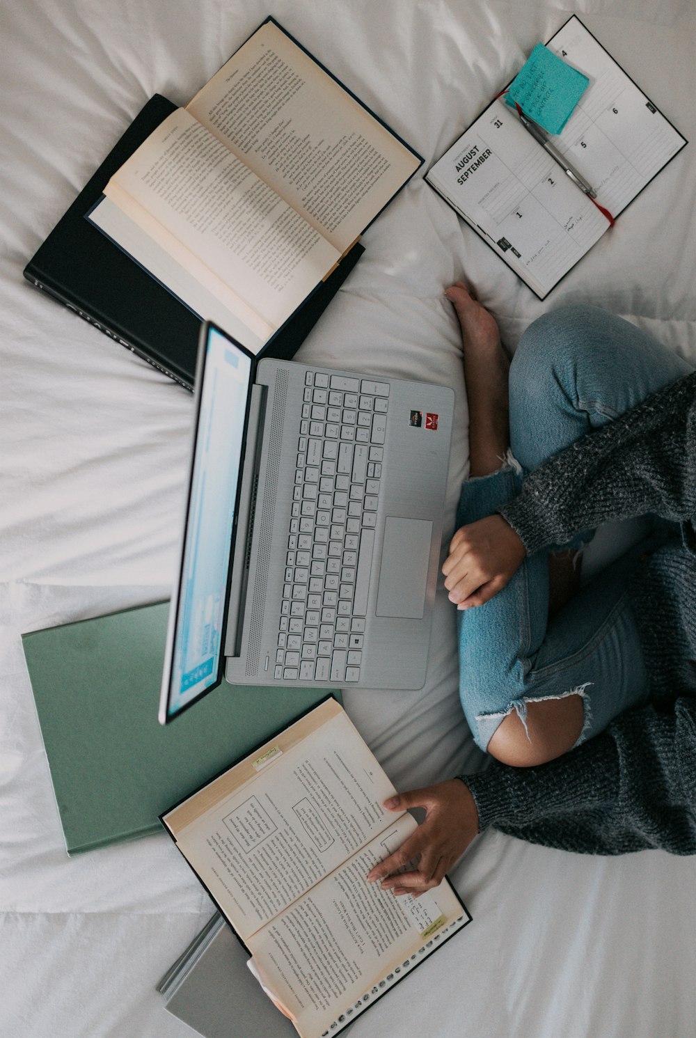 woman in blue long sleeve shirt and blue denim jeans sitting on bed using laptop