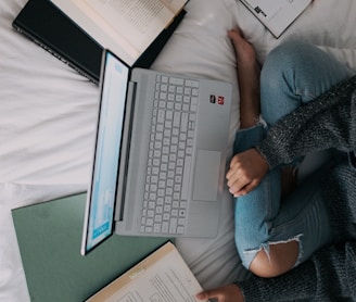 woman in blue long sleeve shirt and blue denim jeans sitting on bed using laptop