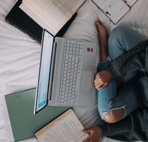 woman in blue long sleeve shirt and blue denim jeans sitting on bed using laptop