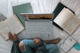 person in blue denim jeans sitting on bed with laptop