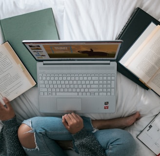 person in blue denim jeans sitting on bed with laptop