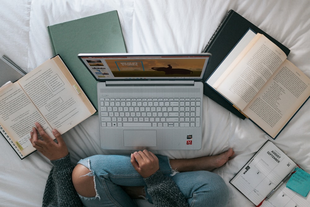 person in blue denim jeans sitting on bed with laptop