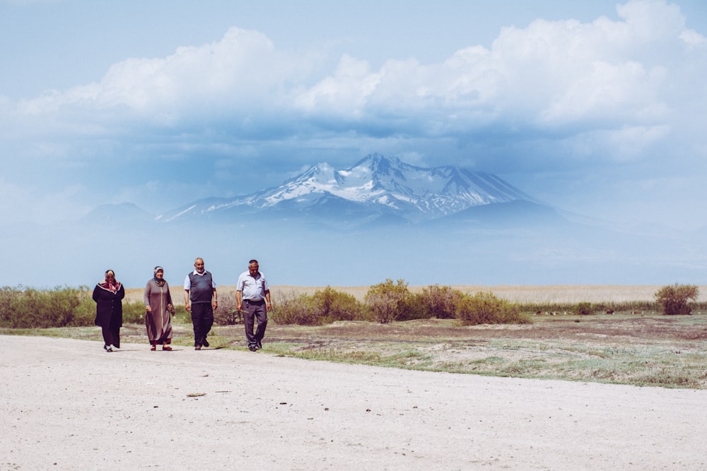 3 men and woman walking on white sand during daytime