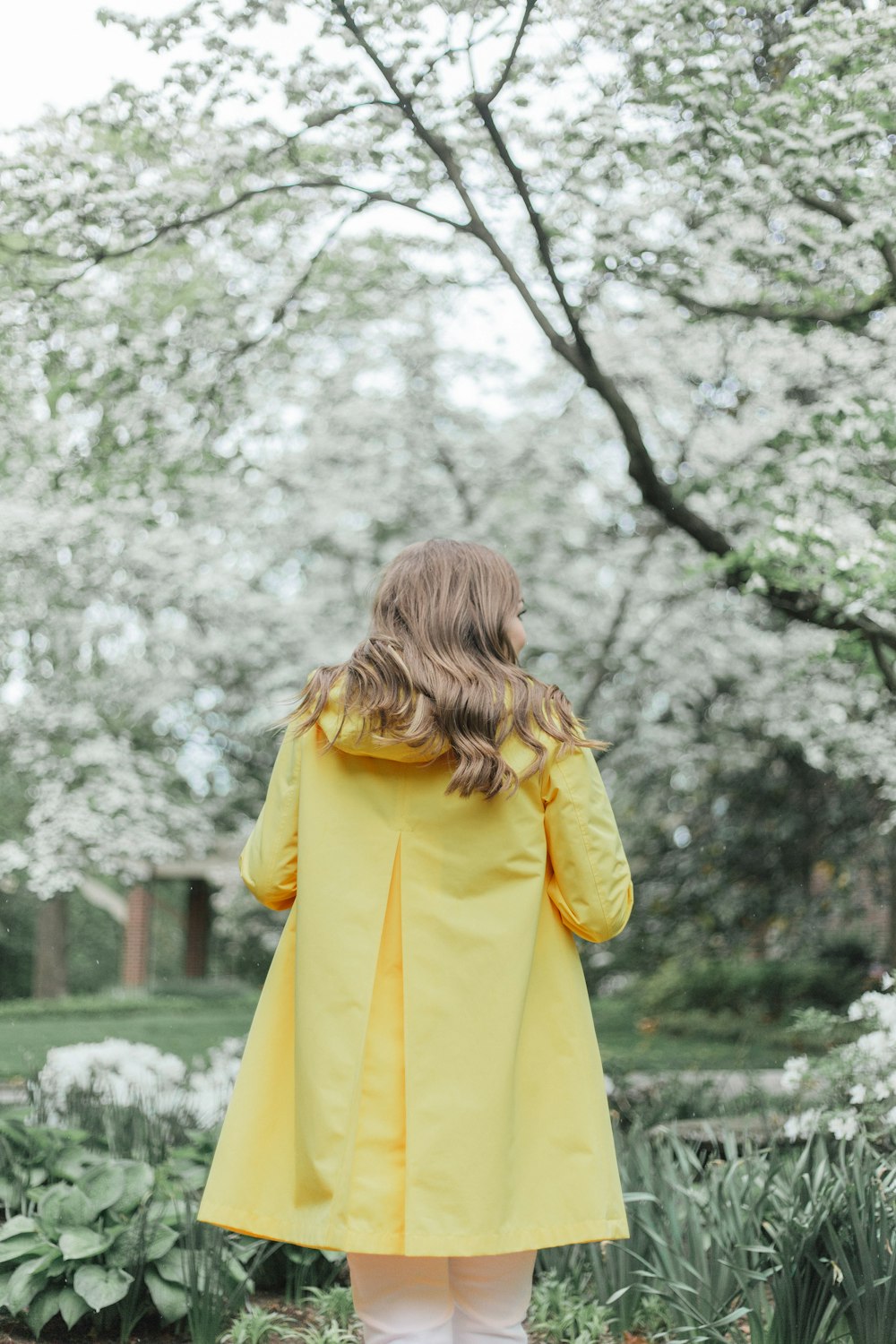 woman in yellow coat standing near trees during daytime