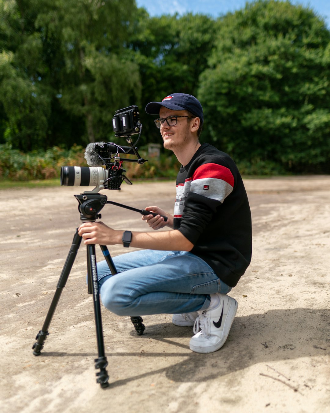 man in black jacket and blue denim jeans sitting on black and gray camera on tripod during