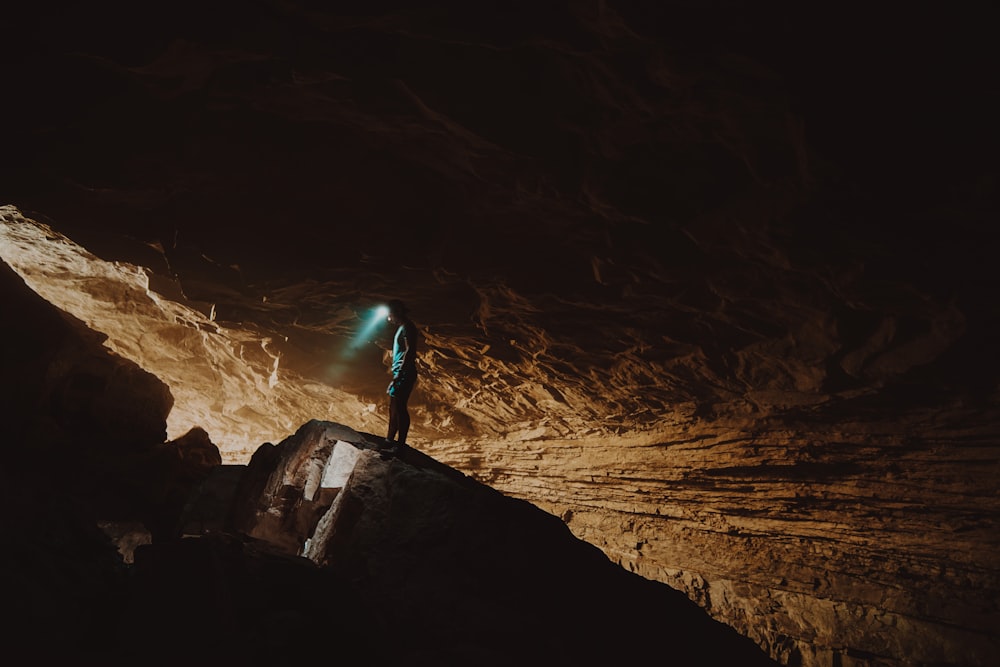 Persona in giacca blu in piedi sulla formazione rocciosa marrone durante il giorno