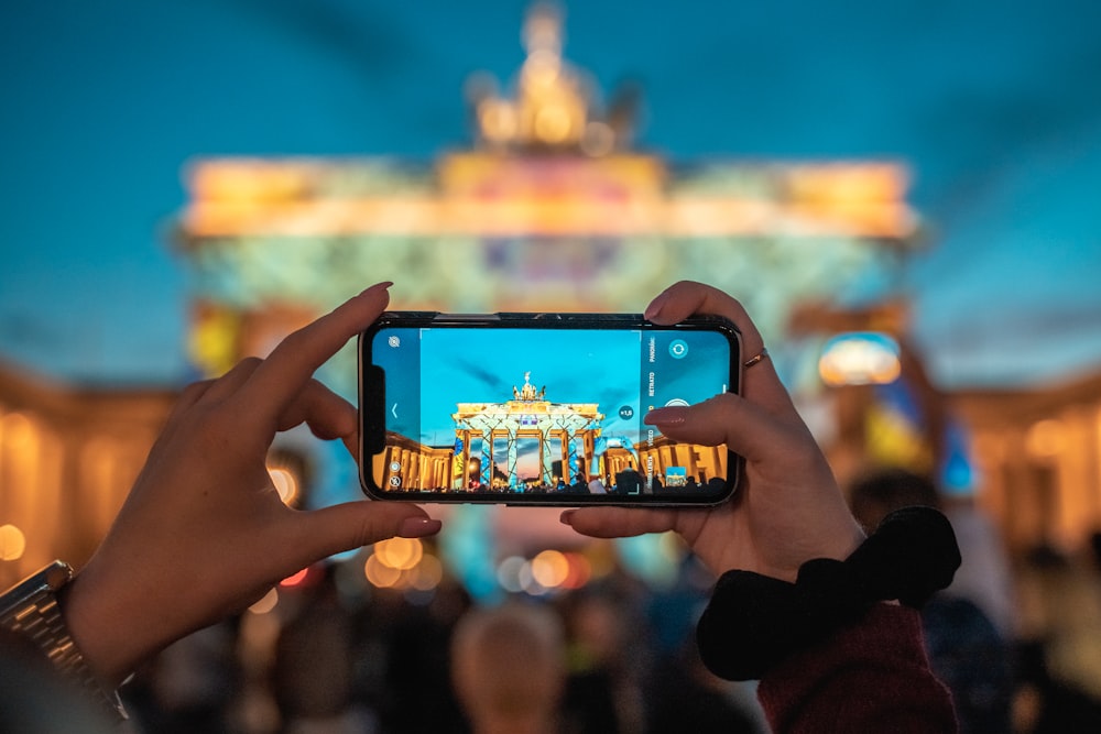 Persona que sostiene un teléfono inteligente negro que toma fotos de los edificios de la ciudad durante el día