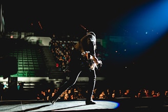 man in black jacket and black pants playing guitar on stage