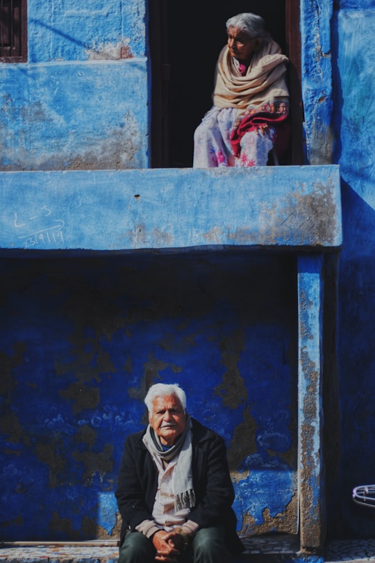 man in black jacket standing beside blue concrete wall in Jodhpur India