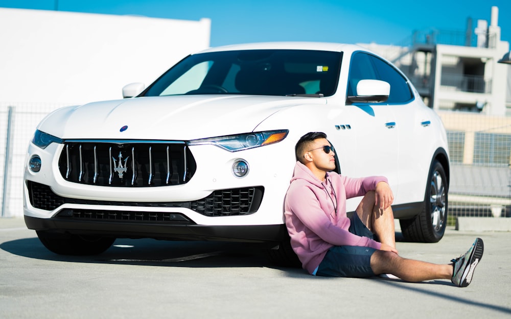 Femme en robe rose assise à côté d’une voiture BMW blanche