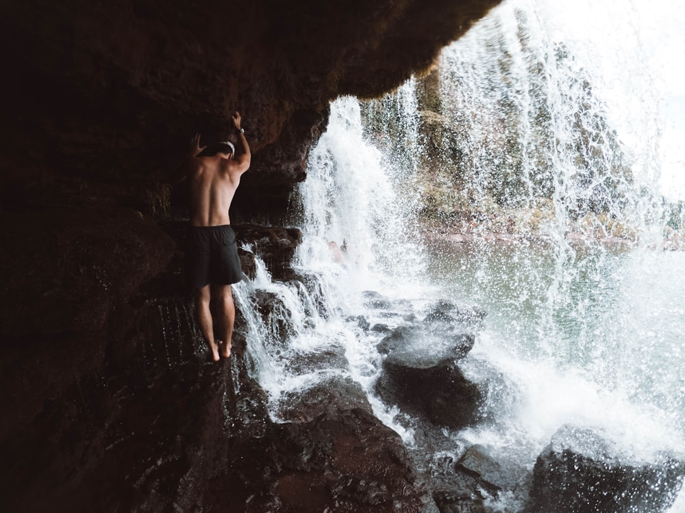 woman in black bikini standing on brown rock near waterfalls during daytime