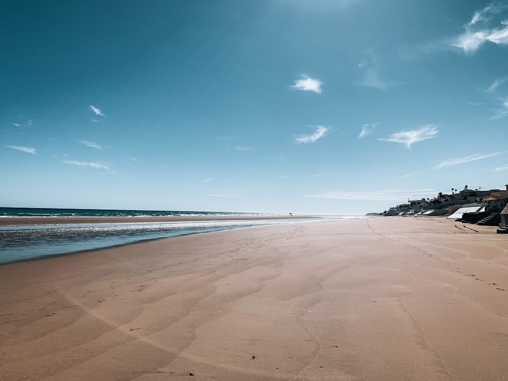 areia marrom perto do corpo de água sob o céu azul durante o dia