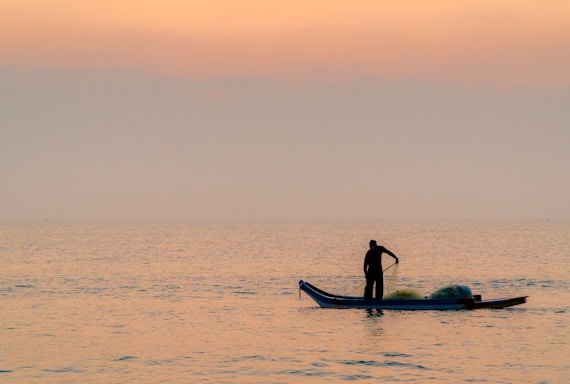 A friendly fisherman writing a message on a laptop by the lakeside at sunset.