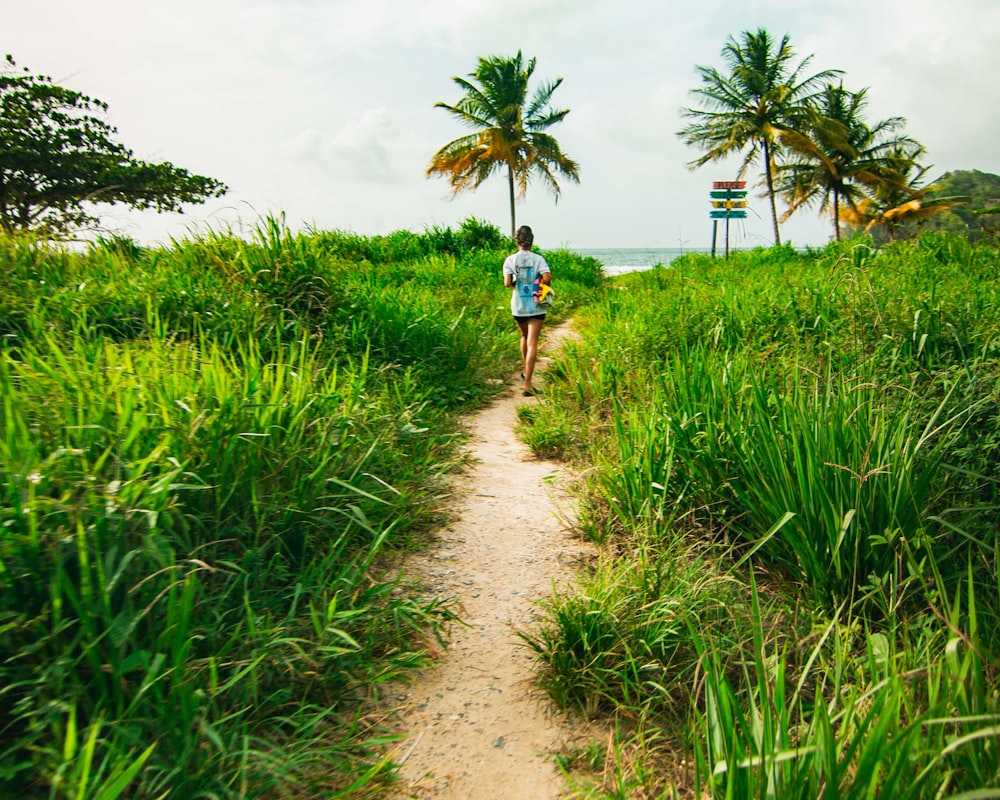 girl in blue shirt walking on pathway between green grass field during daytime